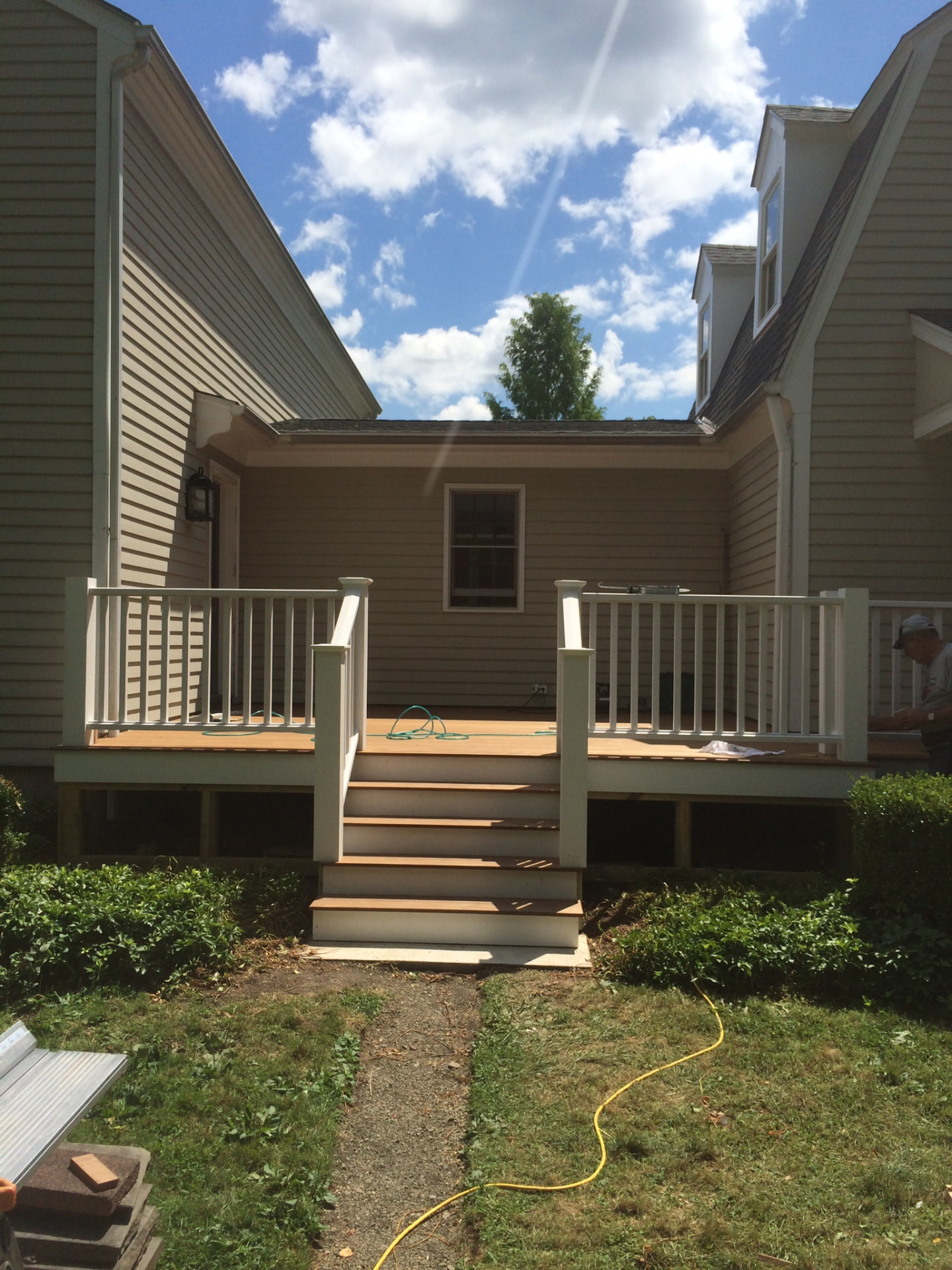 New composite deck with white railings and wide stairs spanning the rear of a country house