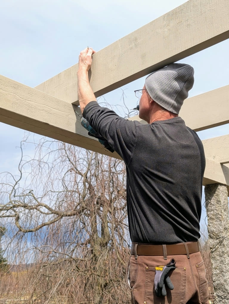 Dmitri lifting and fastening a cedar lintel beam into place beneath the pergola rafters