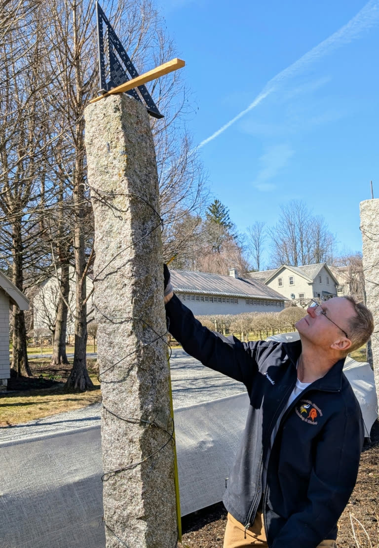 Dmitri holding a speed square and tape measure against a granite post to check plumb